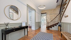 A hallway with a staircase, a round mirror, a console table, and patterned rug. - Holiday Home “La Maison De Famille” with Private Terrace, Garden & Wi-Fi (Luçon)