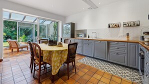 A modern kitchen with grey cabinets, a wooden countertop, and a dining area with a table and chairs. - Holiday Home “La Maison De Famille” with Private Terrace, Garden & Wi-Fi (Luçon)