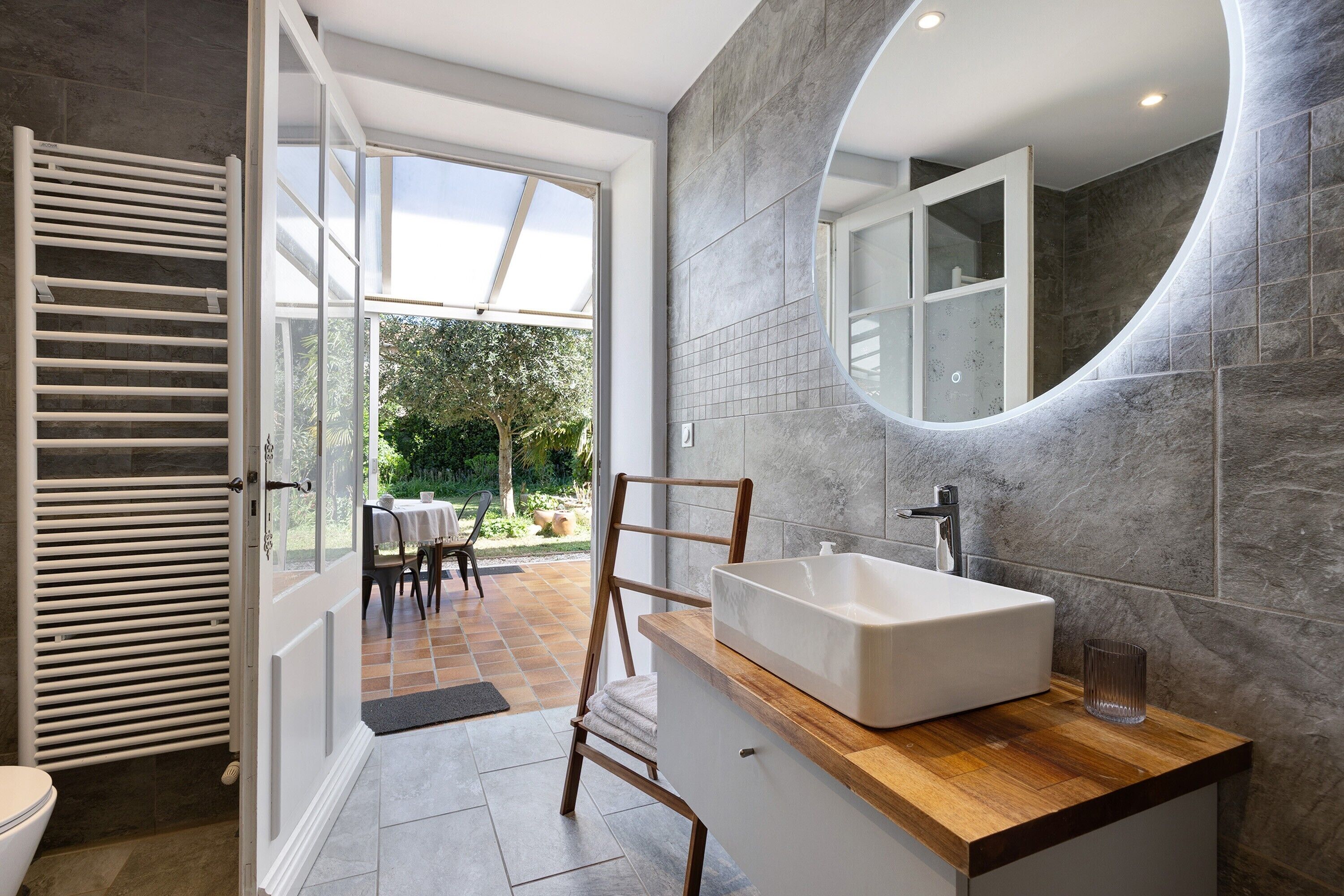 Une salle de bain dotée d’un grand miroir, d’un meuble-lavabo en bois et donnant sur le patio extérieur.
