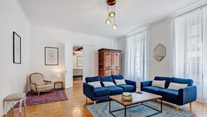 A spacious living room with a blue sofa, a wooden coffee table, a patterned rug, and a wooden cabinet. - Holiday Home “La Maison De Famille” with Private Terrace, Garden & Wi-Fi (Luçon)
