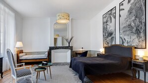 A modern hotel room with a bed, a seating area with a chair and a small table, a mirror, and a large framed artwork on the wall. - Holiday Home “La Maison De Famille” with Private Terrace, Garden & Wi-Fi (Luçon)