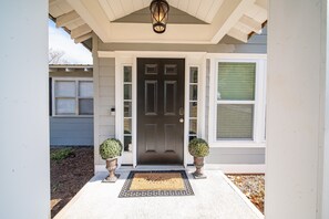 A front entrance with a dark door, white trim, and a welcome mat. - Peaceful Country Home With Stylish Comforts (Hamilton)