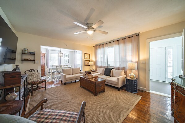 A spacious living room with a ceiling fan, two sofas, a coffee table, and a dining area with a table and chairs. - Peaceful Country Home With Stylish Comforts (Hamilton)