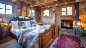 Ein Schlafzimmer einer Holzhütte mit einem großen Bett, einem Kamin und einem Fenster mit Vorhängen.