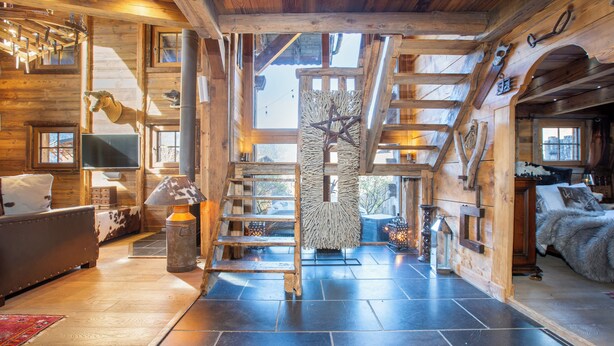 Ein rustikales Blockhaus-Interieur mit Kamin, Holzwänden, einer Treppe und einem an der Wand befestigten Fernseher.