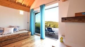 A wooden-framed room with a sofa, a sliding glass door leading to an outdoor area with a chair and a small table. - Baita Pranolz (Borgo Valbelluna)