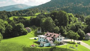 A large house with a red roof, surrounded by lush green fields and trees, set in a hilly landscape. - Baita Pranolz (Borgo Valbelluna)