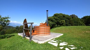 A wooden sauna structure with a chimney, set on a grassy platform with a clear view of the surrounding landscape. - Baita Pranolz (Borgo Valbelluna)