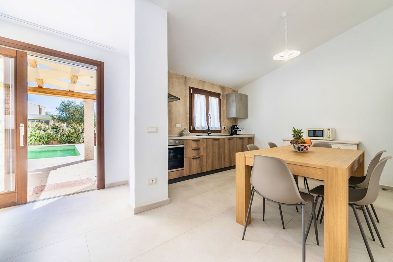 Una cocina moderna con armarios de madera, una mesa de comedor con sillas y vista a una piscina.