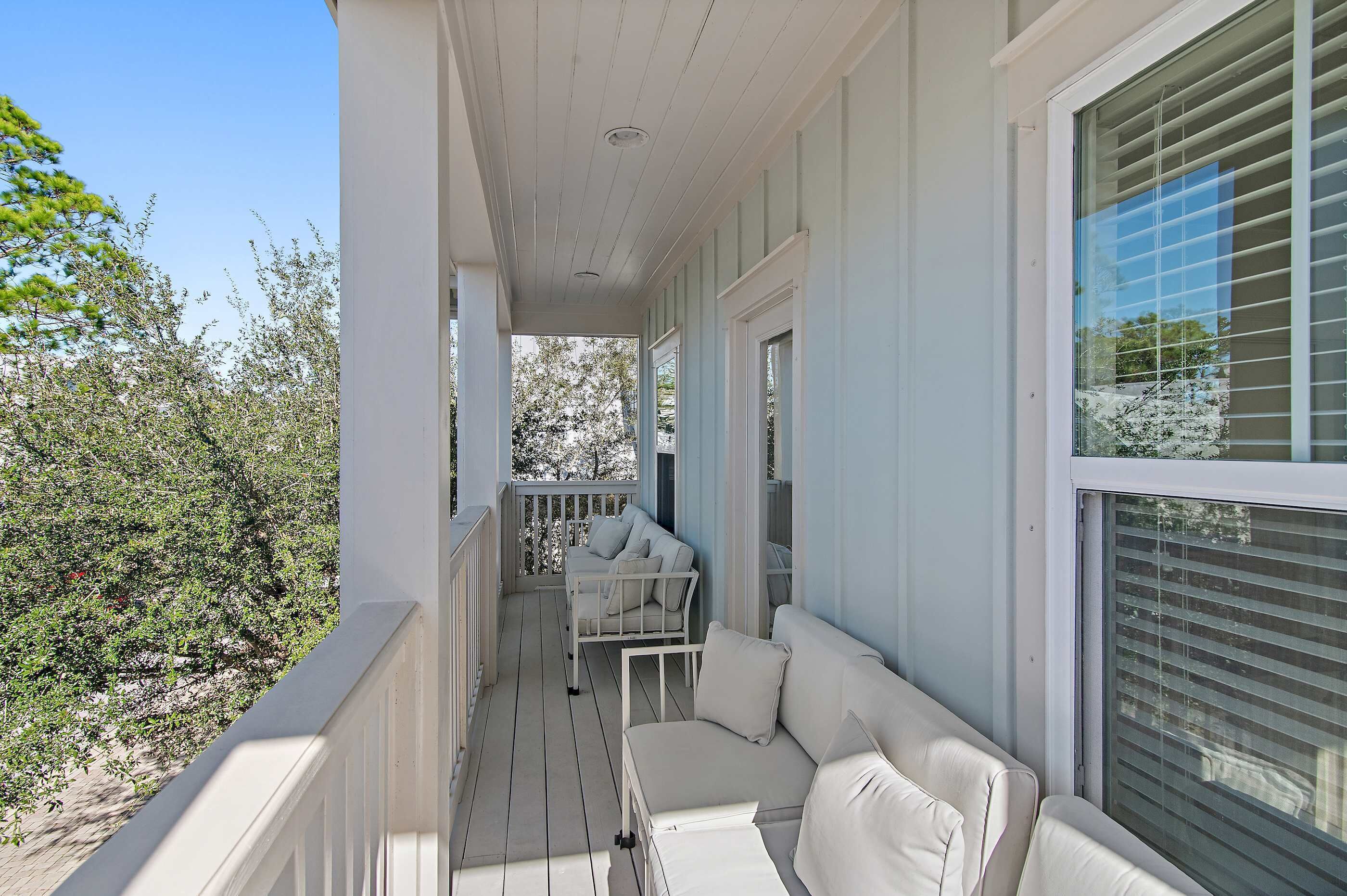 Une véranda avec un canapé blanc et une petite table, entourée de balustrades blanches et offrant une vue sur les arbres.
