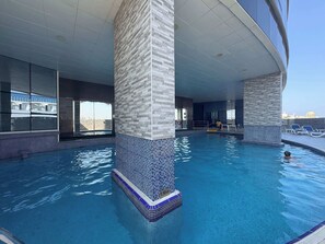 A modern indoor swimming pool with tiled walls and a clear view of the city skyline. - Stayshort - Stylish 1BR Apartment With Stunning Lake Views (Dubai)
