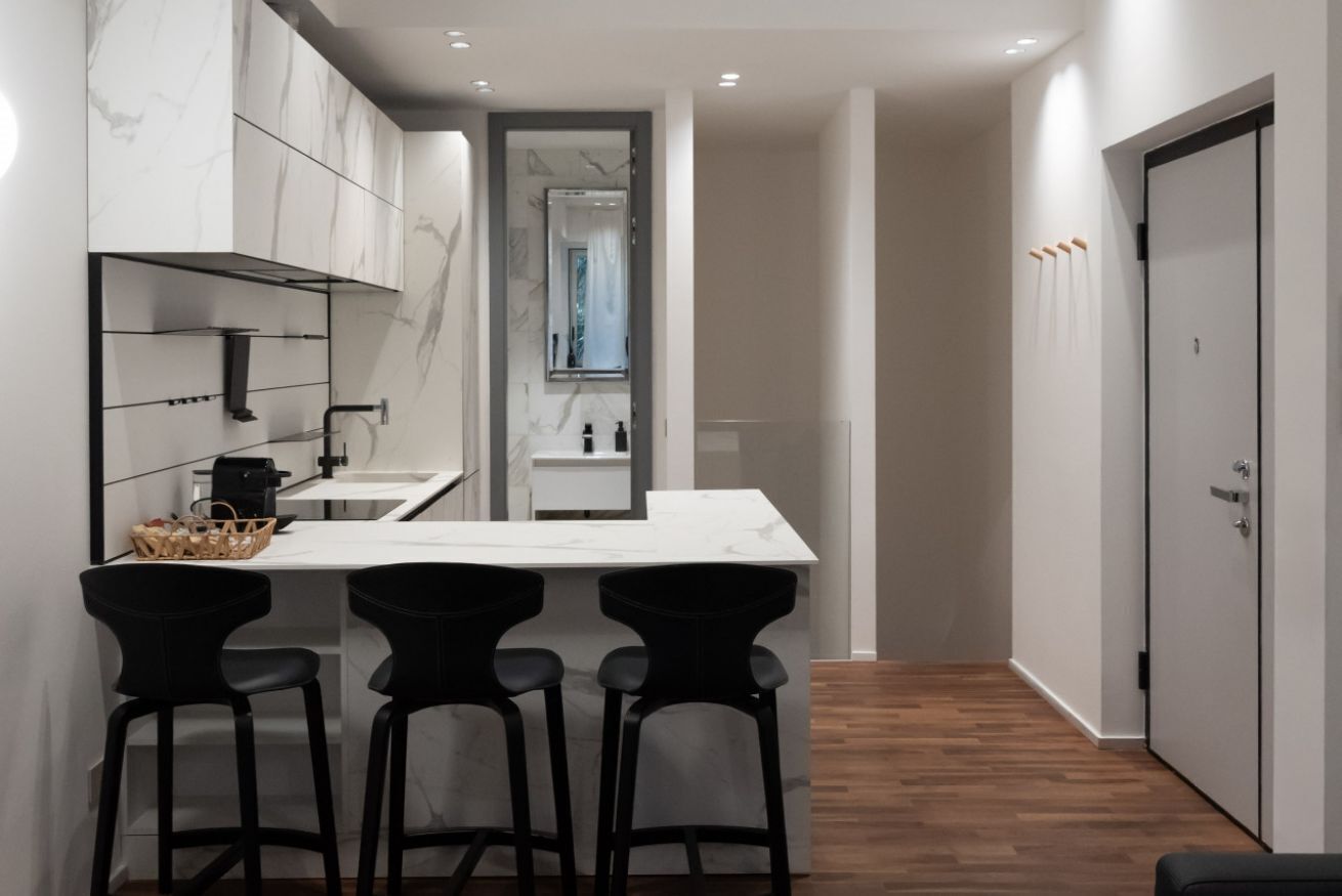 Une cuisine moderne avec un dosseret en marbre, un îlot central doté de tabourets de bar et une vue sur la salle de bain adjacente.