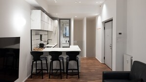 A modern kitchen with a marble backsplash, a central island with bar stools, and a hallway leading to a door. - Refined two-room bedroom between Brera and the Duomo (Milan)