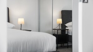 A modern hotel room with a large bed, two bedside tables with lamps, and a full-length mirror. - City Stay Steps From Yarra River Walks (Melbourne)