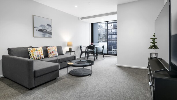 A modern living room with a grey sofa, a coffee table, and a flat-screen TV. - City Stay Steps From Yarra River Walks (Melbourne)