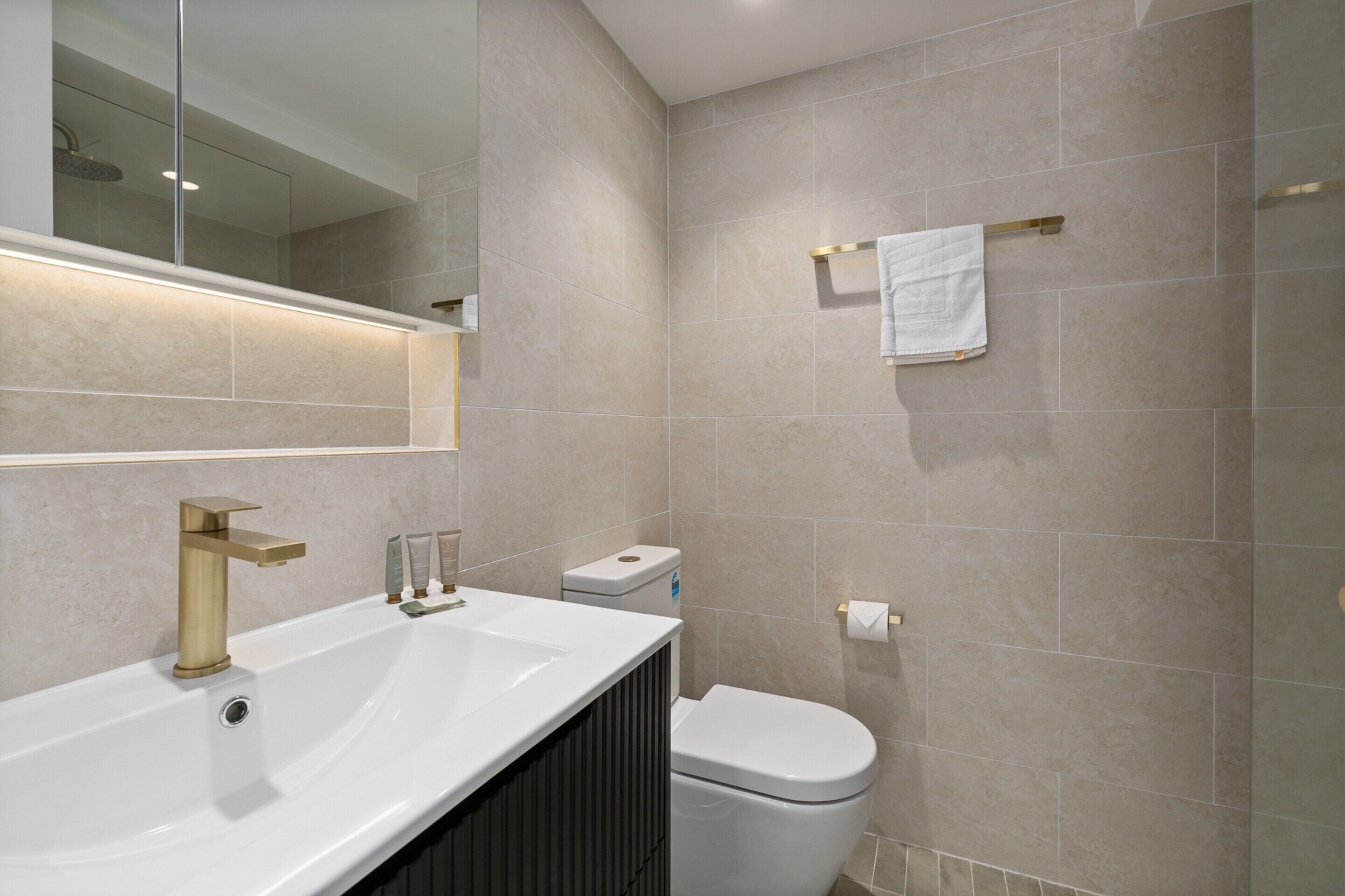 A modern bathroom with a white sink, gold faucet, and a toilet.