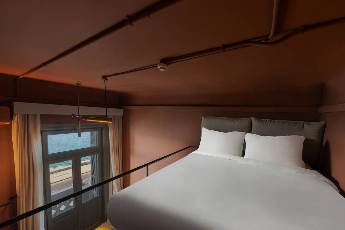 Een hotelkamer met een bed, een raam met gordijnen en uitzicht op zee.