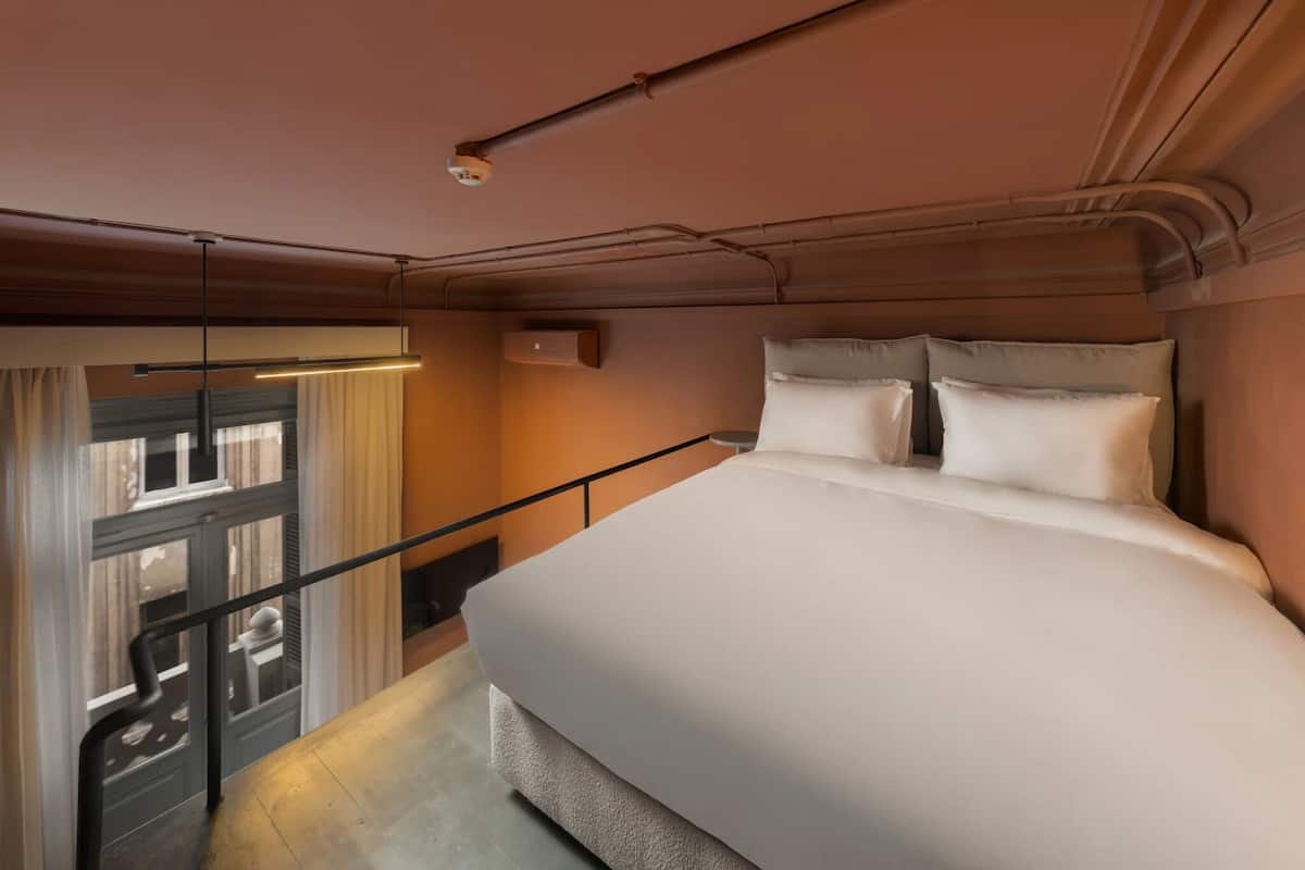 Een slaapkamer met een bed, een raam met gordijnen, een leuning en een plafondlamp.