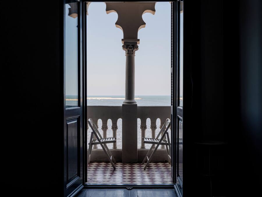 An open doorway leading to a balcony with a checkered floor and two chairs.