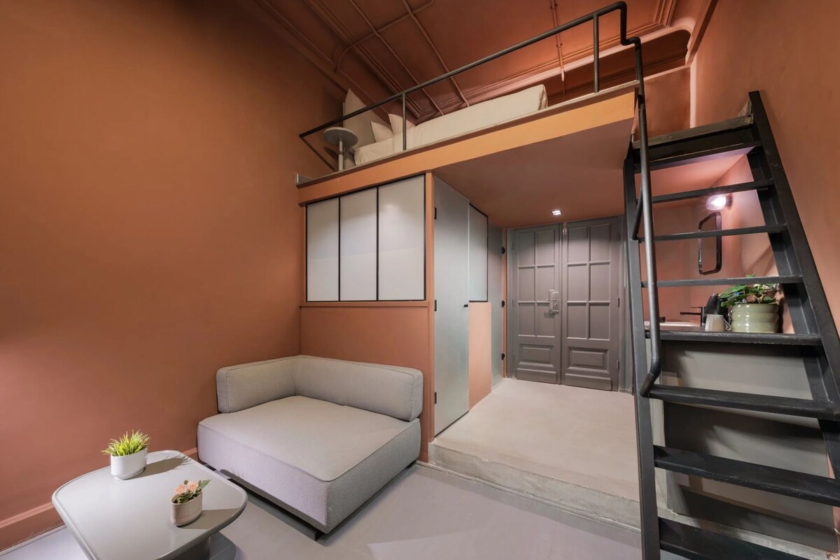 Ein kleines Zimmer mit Schlafkoje, einer Schlafcouch, einem kleinen Tisch mit Pflanzen und einer Treppe.