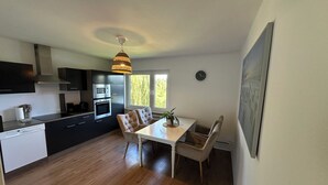 A modern kitchen with dark cabinetry, a white countertop, and a dining area with a table and chairs. - House Königsee *garden view (Bad Oldesloe)