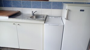 Eine Küche mit Spüle, Schneidebrett aus Holz und Kühlschrank in Weiß.