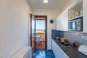 Een kleine keuken met uitzicht op zee, een eethoek met tafel en stoelen, en een magnetron op het aanrecht.