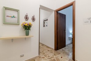 A hallway with a wooden door, a framed welcome sign, a decorative wall piece, and a vase with flowers.