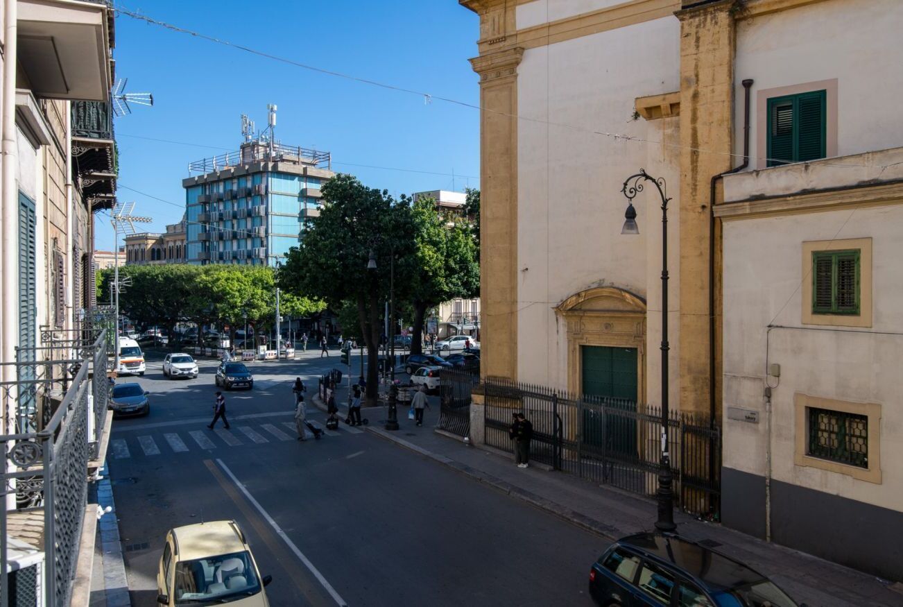 Vista da rua com edifícios, uma faixa de pedestres e carros.