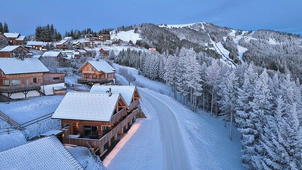 Un pueblo cubierto de nieve con edificios de madera, una pista de esquí y un cielo despejado.