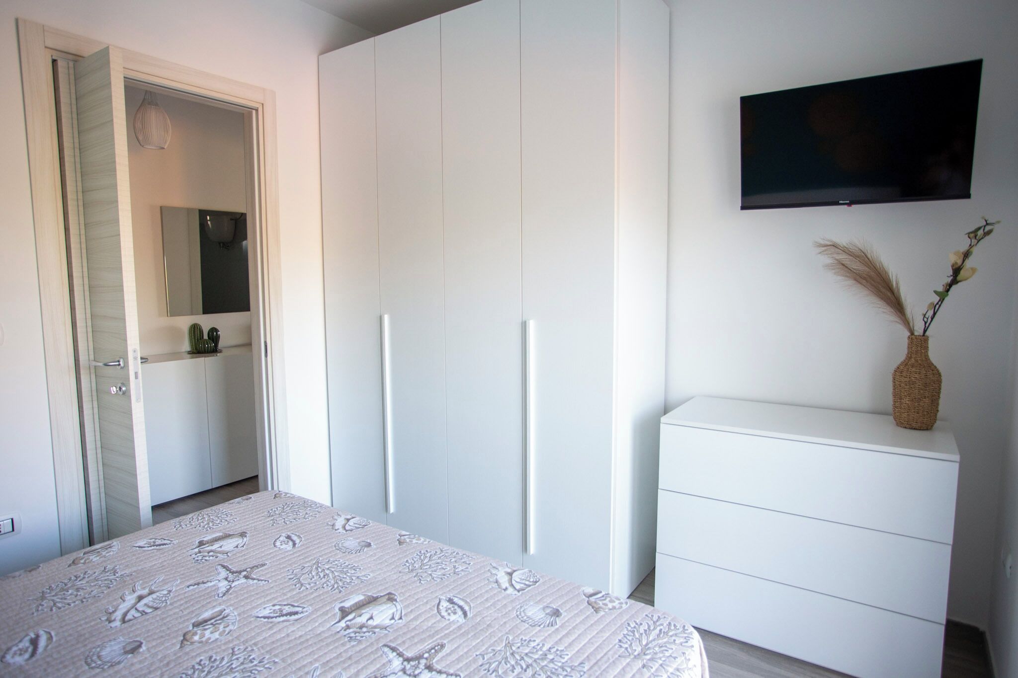 A bedroom with a bed, a wardrobe, a dresser, and a TV on the wall.