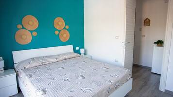 Un dormitorio con una pared de acento color turquesa, una cama con colcha de estampado floral y una mesita de noche blanca con lámpara.