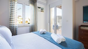 Une chambre d’hôtel avec un lit, une fenêtre avec des rideaux, un balcon et une commode en bois.