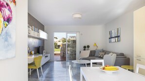 Un salon moderne avec un canapé, une table à manger et des chaises. On trouve une bibliothèque et un téléviseur sur le côté gauche.