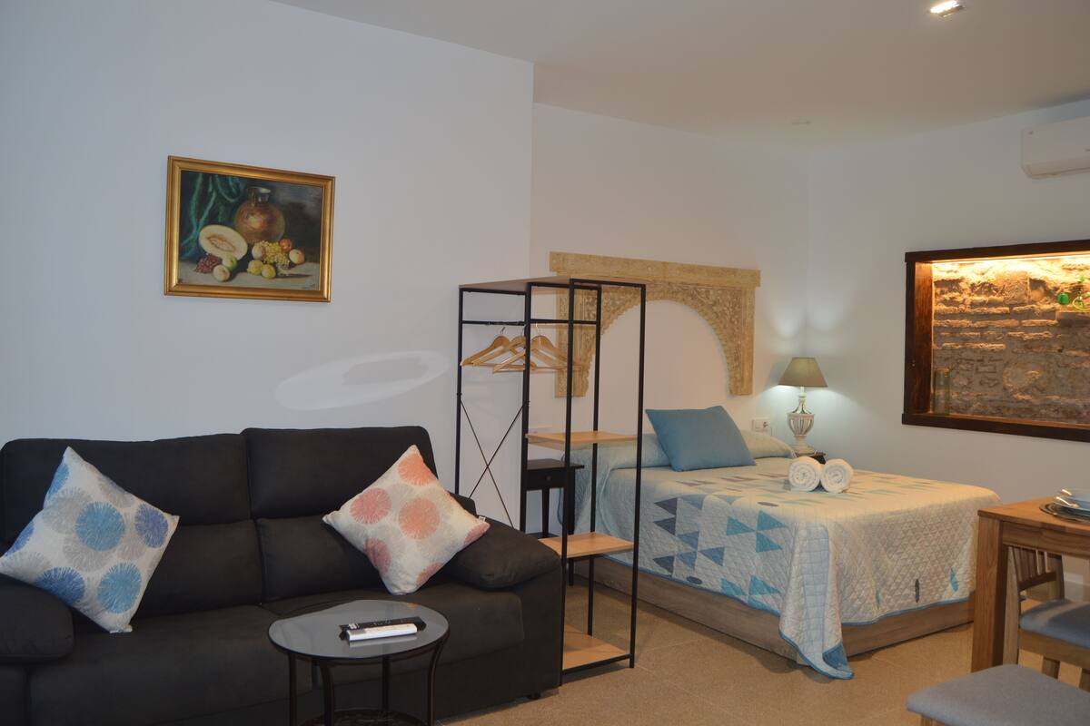 A room with a bed, a sofa, a small table, and a painting on the wall.