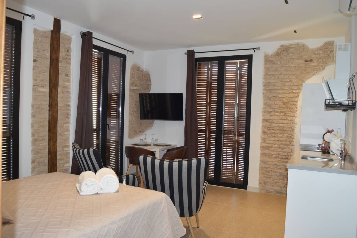 A hotel room with a bed, a small table, a TV, and a kitchenette.