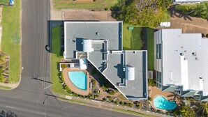 Ett flygbildsbild av ett bostadsområde med ett hus som har en stor swimmingpool, ett garage och en välskött gräsmatta.