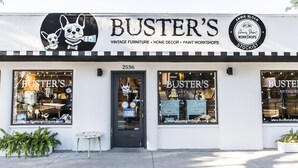 Une devanture de magasin portant le nom « Buster's » et une enseigne indiquant qu'il vend des meubles anciens, des articles de décoration intérieure et propose des ateliers de peinture.
