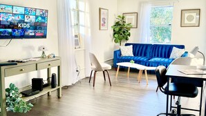 Un salon avec un téléviseur diffusant des émissions pour enfants, un canapé bleu, un bureau avec un ordinateur et une plante.