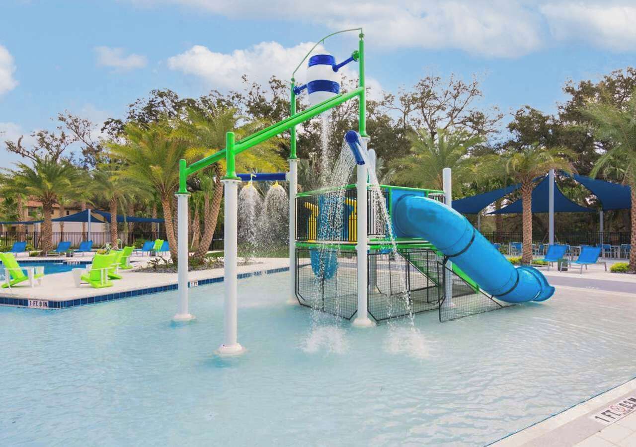 A water park with a blue slide, a water play structure, and a pool area with lounge chairs.
