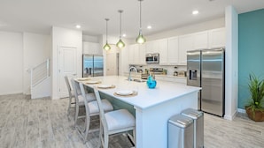 A modern kitchen with white cabinets, stainless steel appliances, and a central island with seating. - Upstay - Magic Mansion w Pool-spa-cinema-games (Kissimmee)