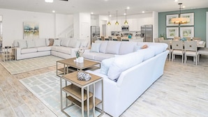 A modern living room with a sectional sofa, a coffee table, and a dining area with a chandelier. - Upstay - Magic Mansion w Pool-spa-cinema-games (Kissimmee)