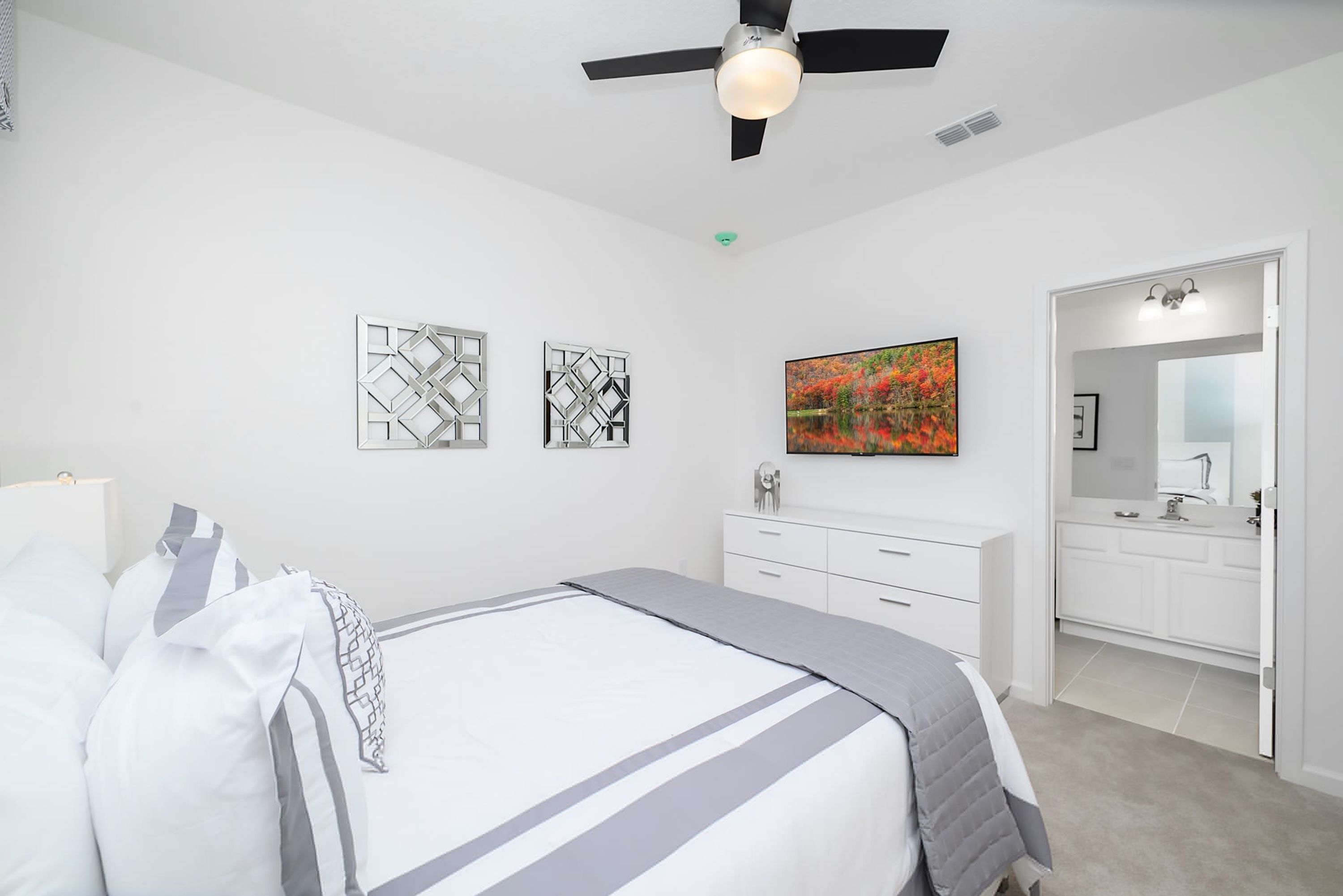 A bedroom with a bed, a dresser, a vanity with a mirror, and a ceiling fan.