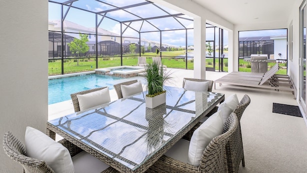 A glass-enclosed patio with a pool, wicker furniture, and a barbecue area. - Upstay - Magic Mansion w Pool-spa-cinema-games (Kissimmee)