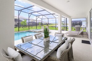 A glass-enclosed patio with a pool, wicker furniture, and a barbecue area. - Upstay - Magic Mansion w Pool-spa-cinema-games (Kissimmee)