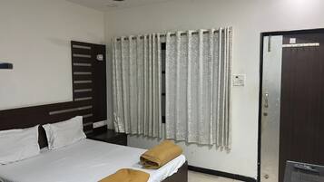 A hotel room with a bed, a ceiling fan, a window with curtains, and a door.