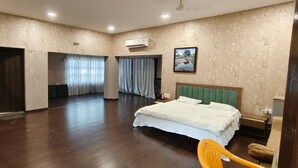 A spacious hotel room with a large bed, a wardrobe, a mirror, and a bathroom with a shower and toilet.
