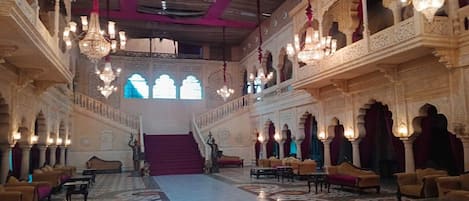 A grand hall with ornate chandeliers, a central staircase, and patterned flooring.