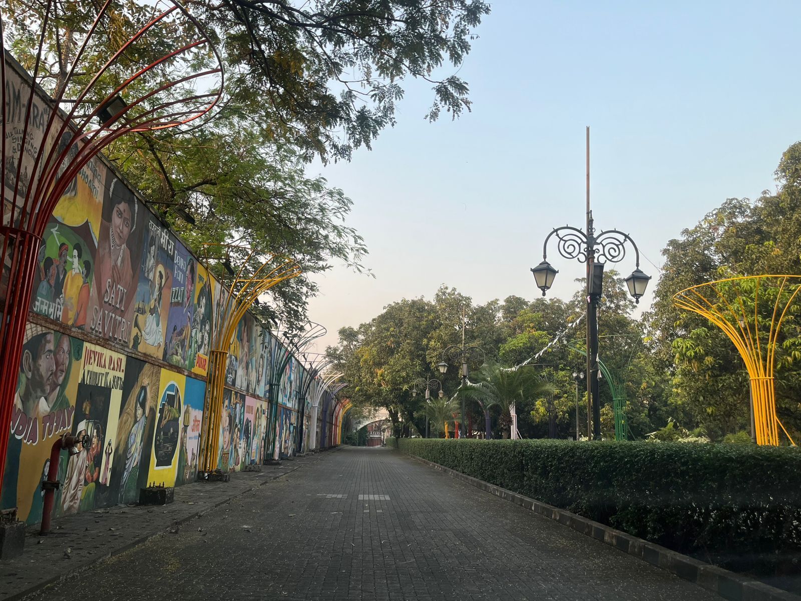 A pathway lined with colorful murals and street lamps, leading towards a distant archway.
