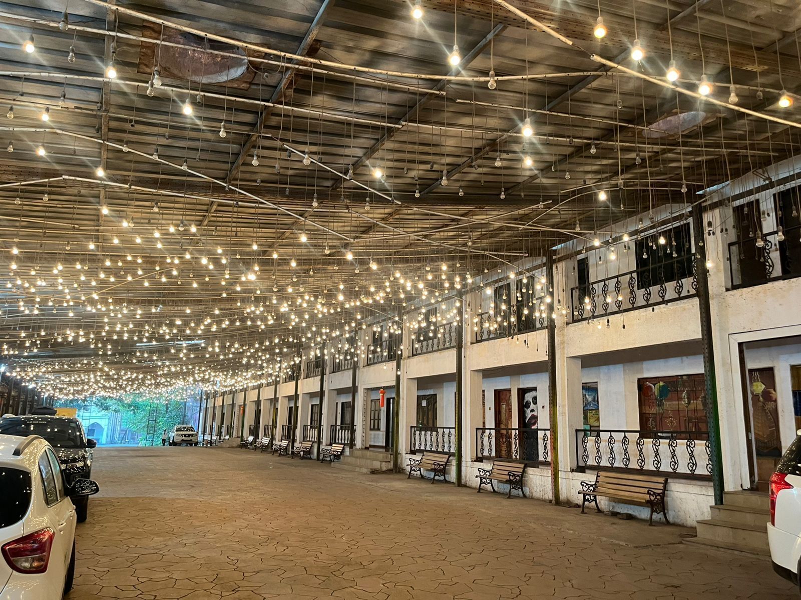 Um espaço amplo e interno, com teto alto decorado com diversas luminárias pendentes, bancos ao longo das paredes e piso revestido de azulejos.